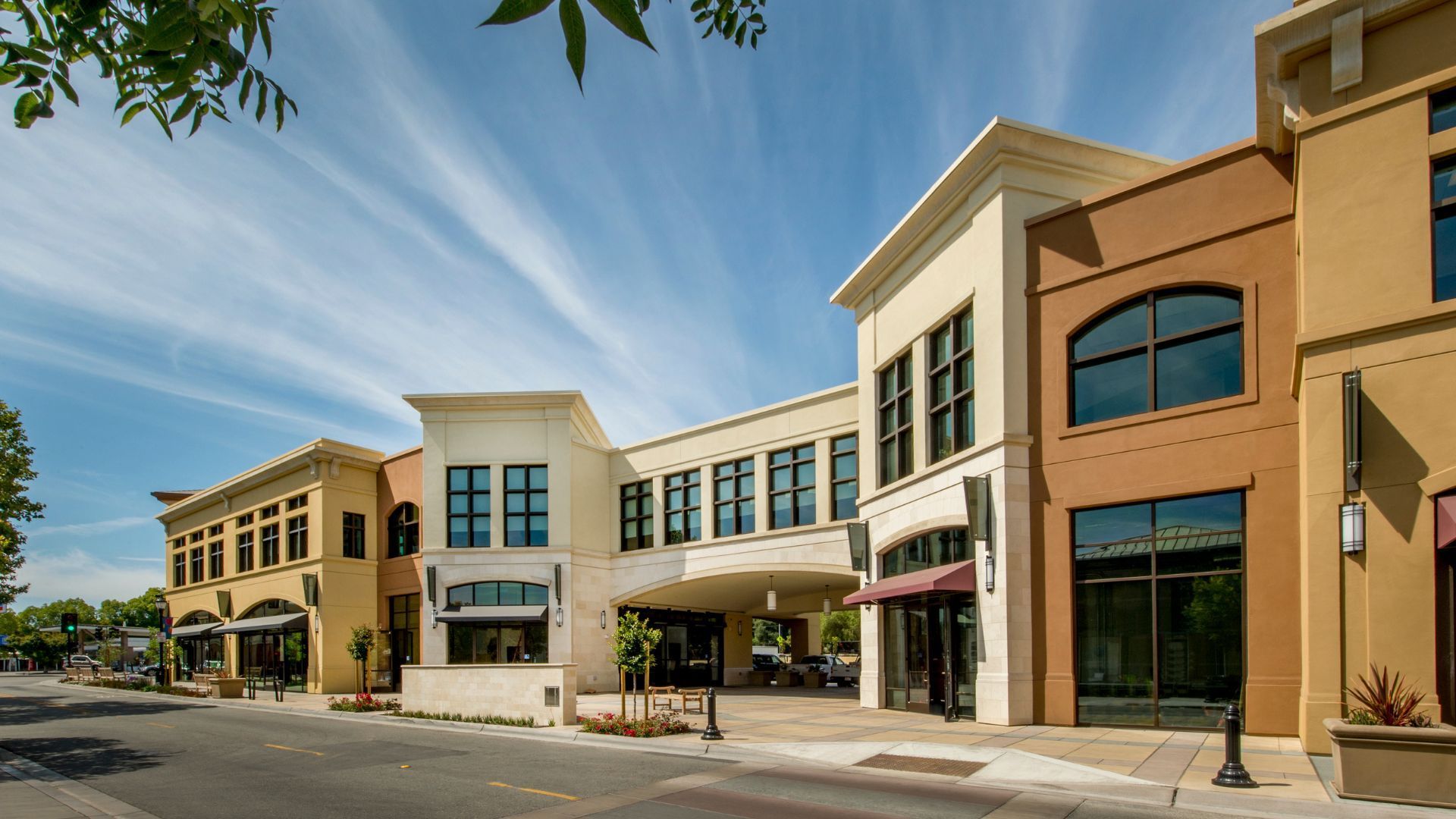 Street view of multi-colored retail buildings under a blue sky with wispy clouds.