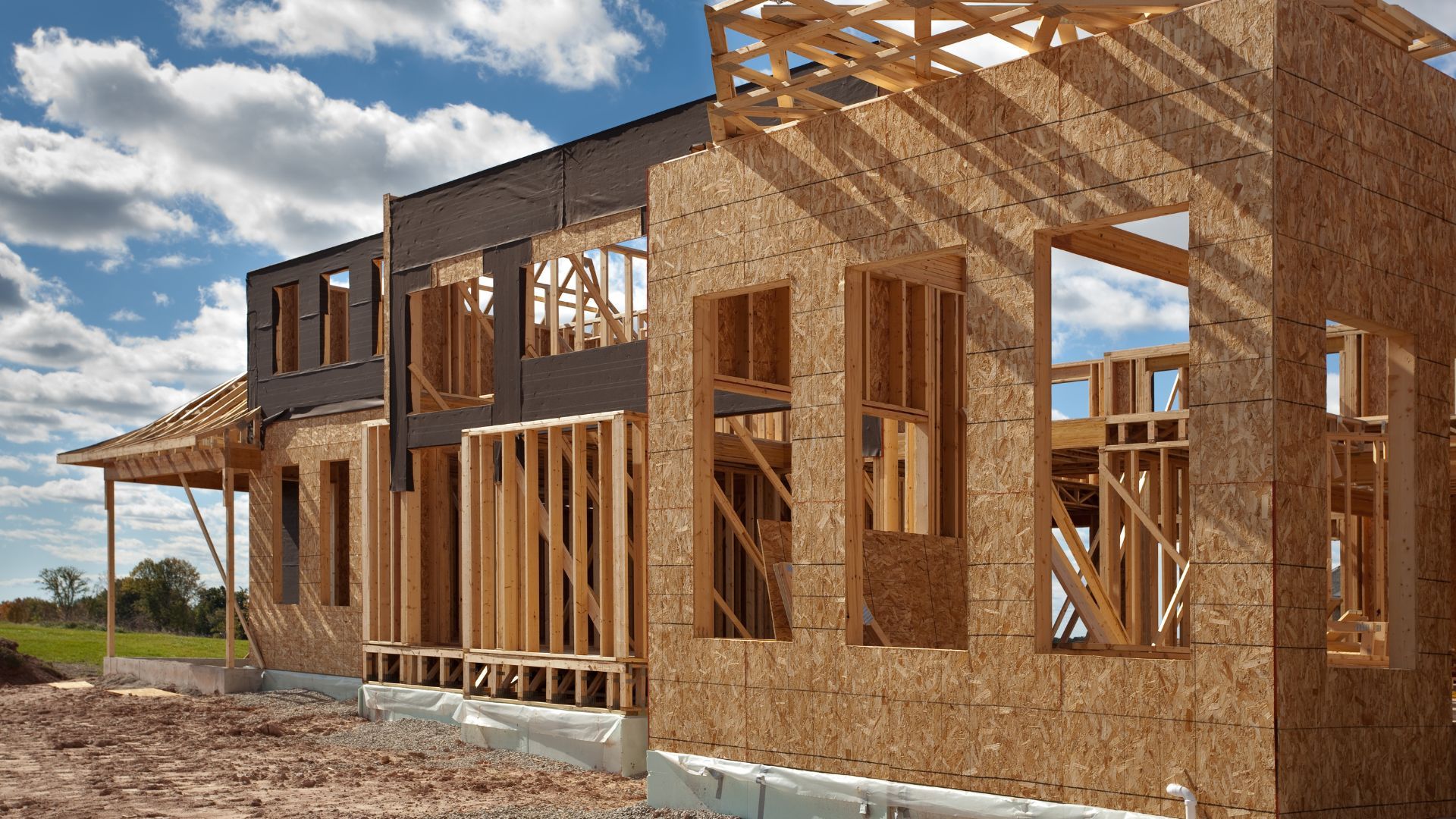 Framing of a house under construction with oriented strand board siding. Blue sky, clouds.
