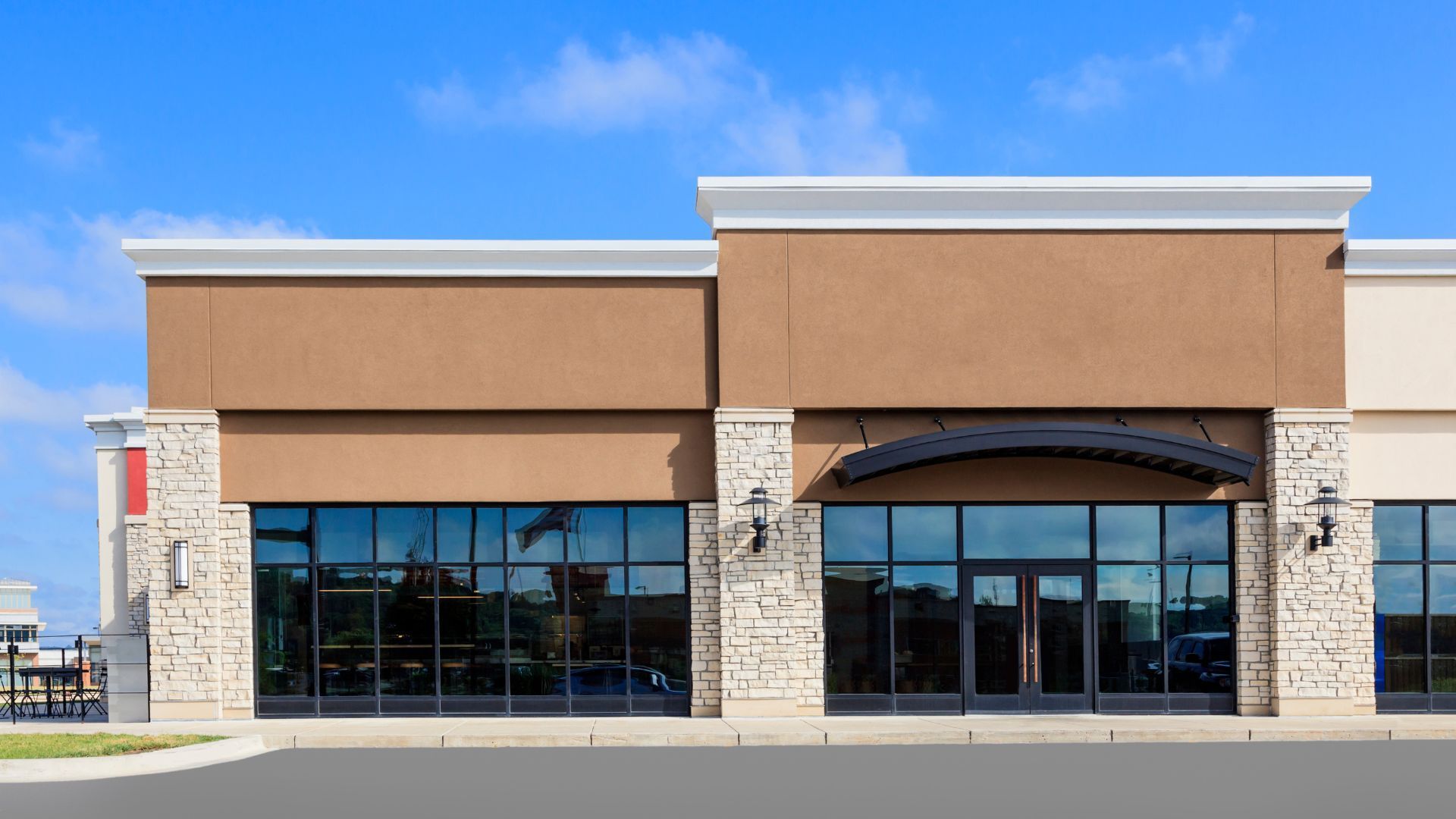 Commercial building exterior with large windows, brown facade, stone accents, and blue sky.