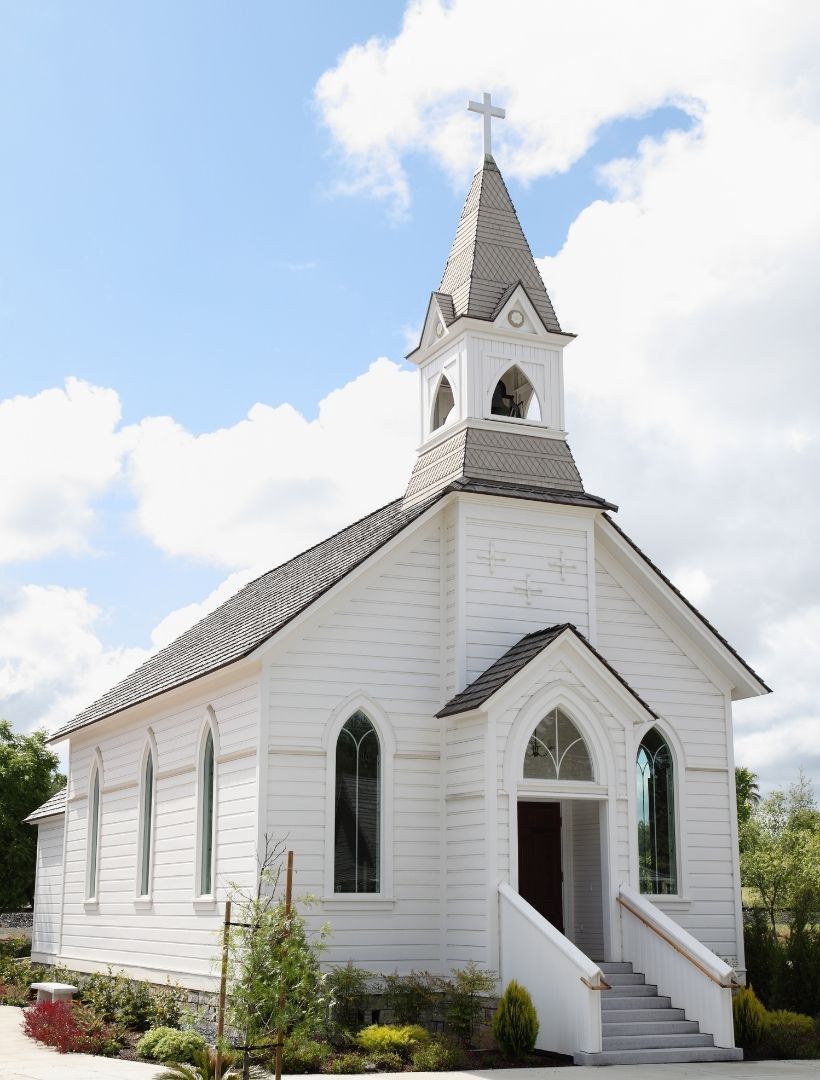 White church with red cross on the front; steeple rises toward a cloudy sky.