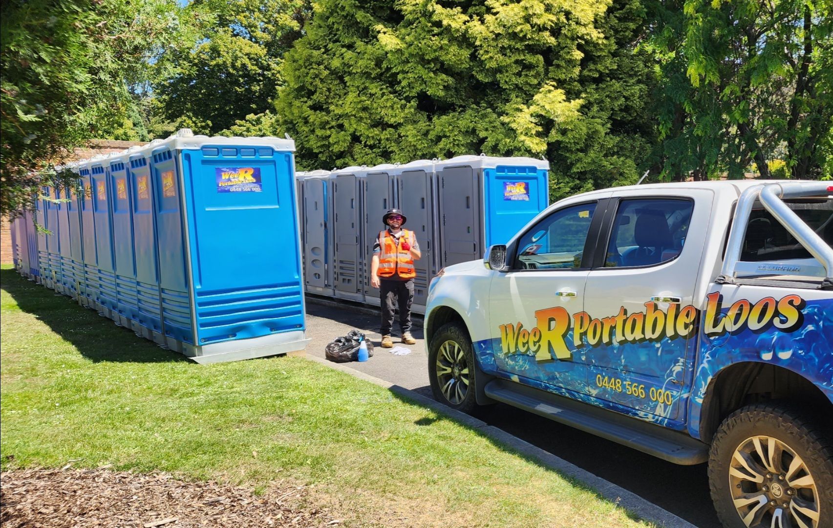 Blue portable toilets lined up on grass beside a white service truck and worker in an orange vest — Wee R Pumping In Glenorchy, TAS