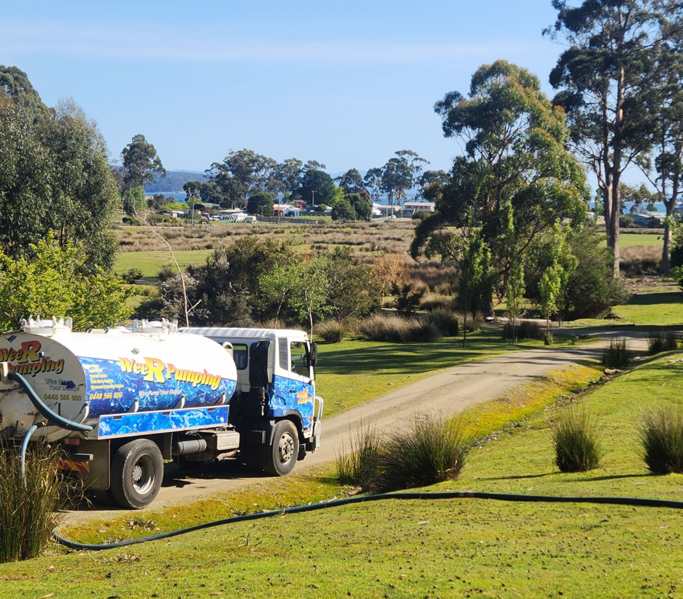 Blue truck carrying a water tank drives along a dirt road through a grassy rural landscape. — Wee R Pumping In Glenorchy, TAS