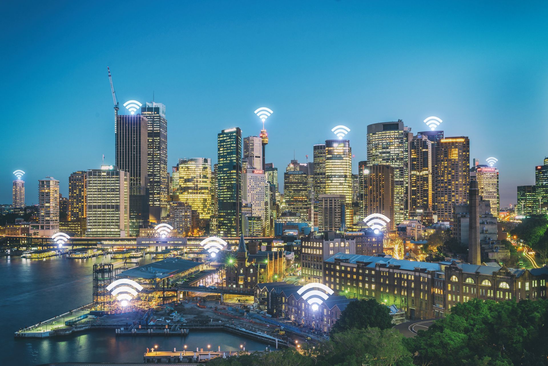 City skyline at night with Wi-Fi symbols overlaid. Buildings lit up, waterfront view.