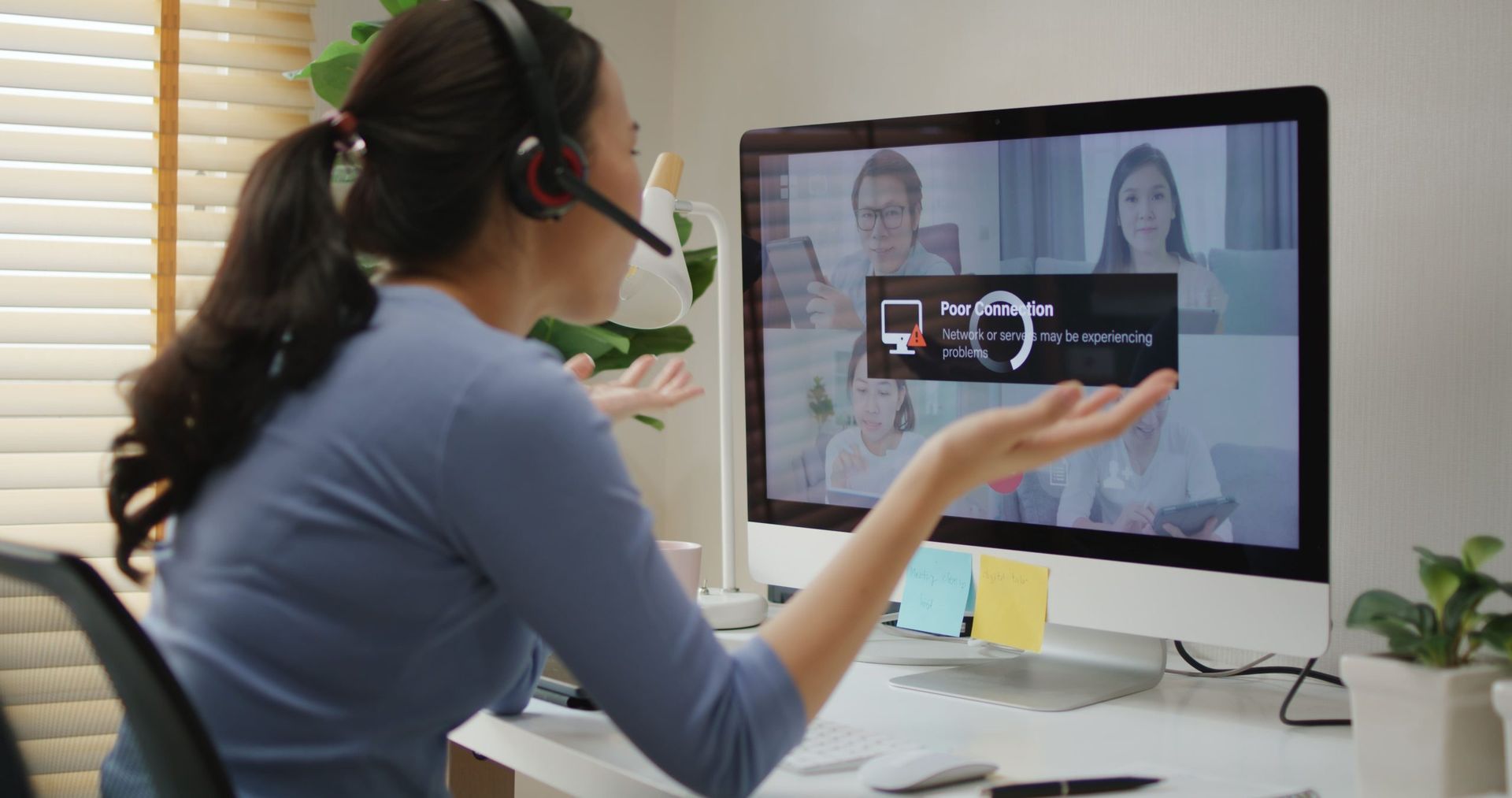 Woman in video call, gesturing with frustration at buffering screen on a computer in home office.