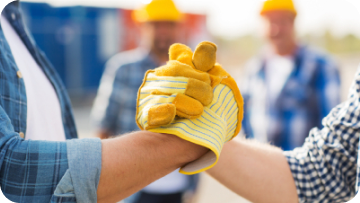 Two construction workers bump gloved hands, others in background.