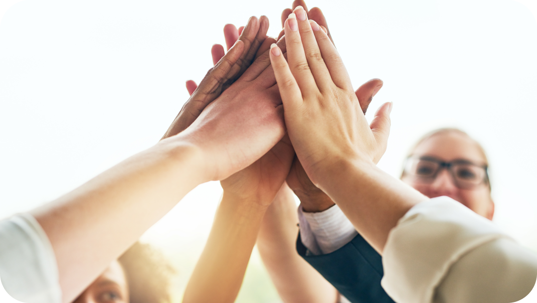 Hands of diverse people in a high-five, celebrating a success, with bright light in the background.