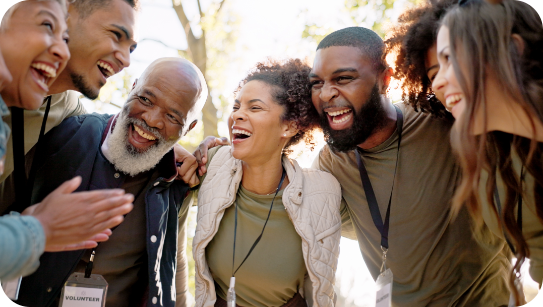 Group of diverse people laughing together outdoors, arms around each other, joyful expressions.