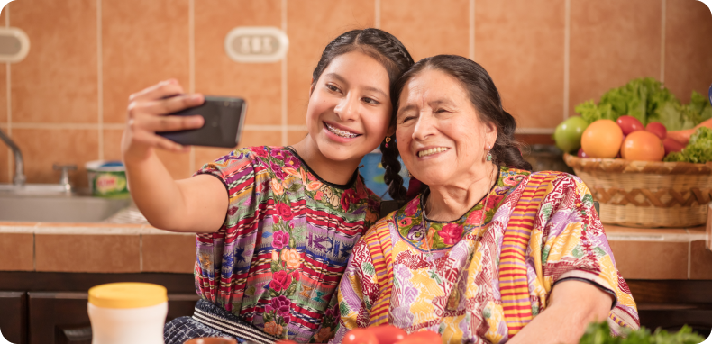 Young woman taking a selfie with an older woman in a kitchen, both smiling.