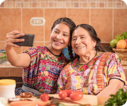 Young woman and older woman in colorful blouses taking a selfie in a kitchen. Young woman and older woman in colorful blouses taking a selfie in a kitchen.