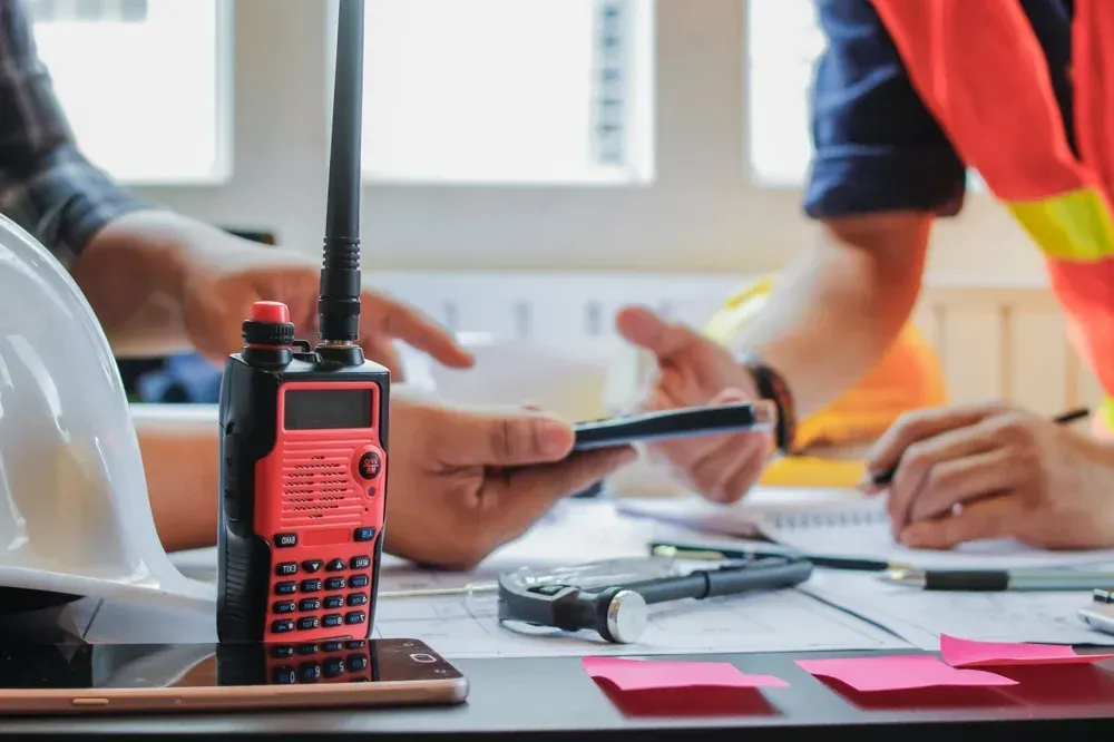 Close-up: Radio on desk, two people discussing plans. Construction site, workspace.