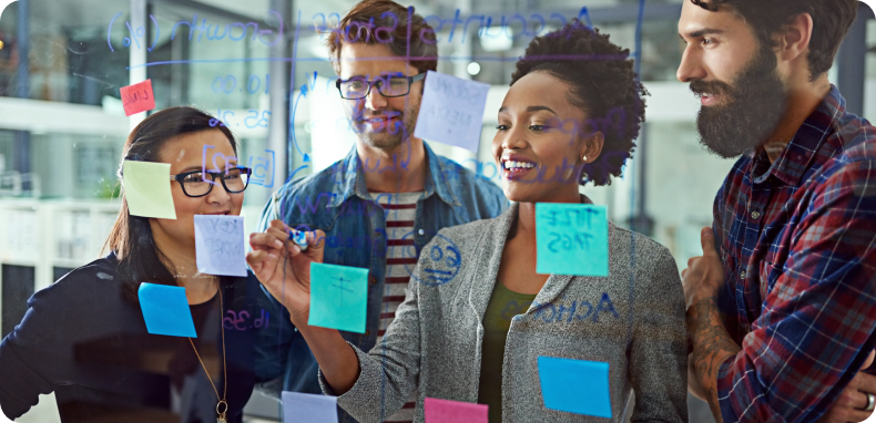 Four people in a collaborative brainstorming session, using sticky notes on a glass wall.