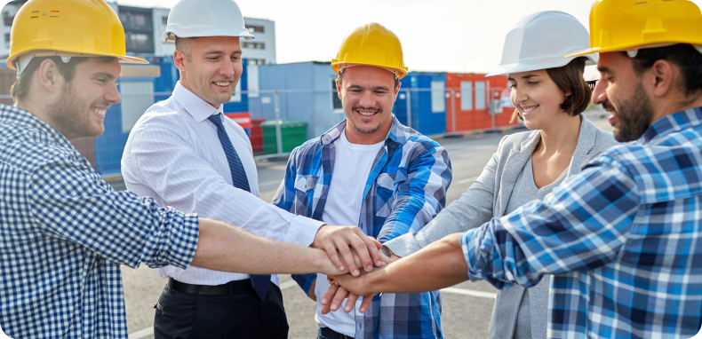 Construction workers in hard hats join hands in a team huddle.