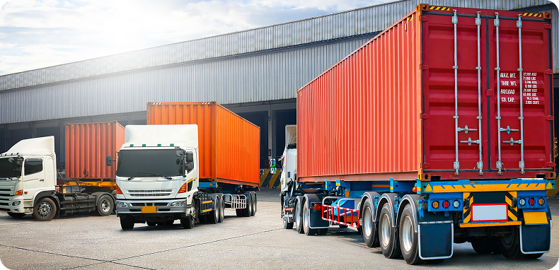 Trucks carrying shipping containers parked near a loading dock.