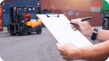 Person writing on clipboard in a warehouse, forklift in background.