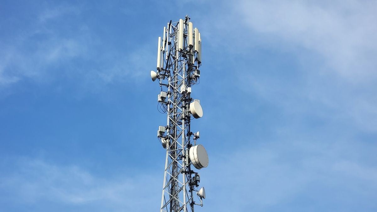Cell tower against a blue sky with white clouds; metal structure with various antennas and equipment.
