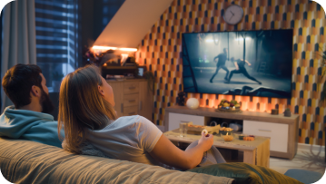 Couple on sofa watching action movie on TV, warm-lit room.