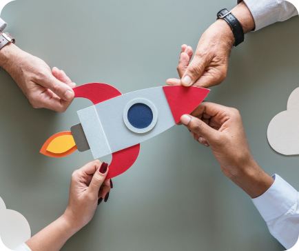 Hands holding a paper rocket, symbolizing teamwork and launch against a gray background with clouds.