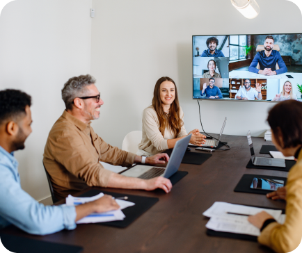 People in a meeting room having a video call with remote colleagues on a large screen.