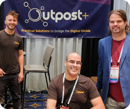 Three men at the Outpost+ booth. Banner says 