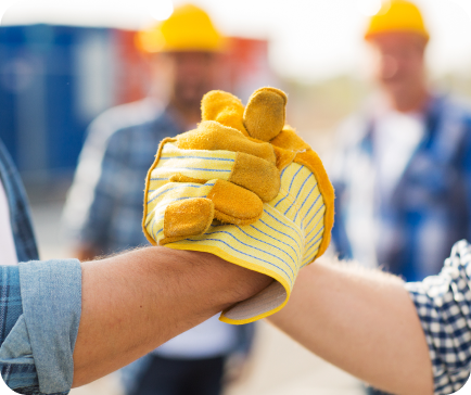 Three construction workers doing a fist bump, one with a work glove, on a construction site.