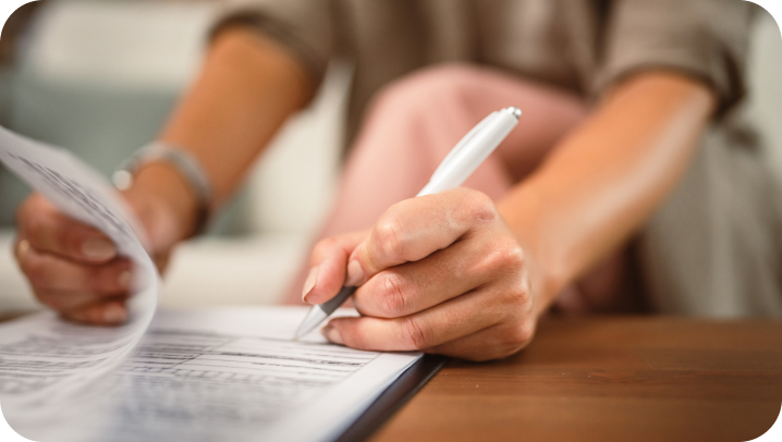 Woman writing on a document with a white pen, focusing on the writing hand and the paper.