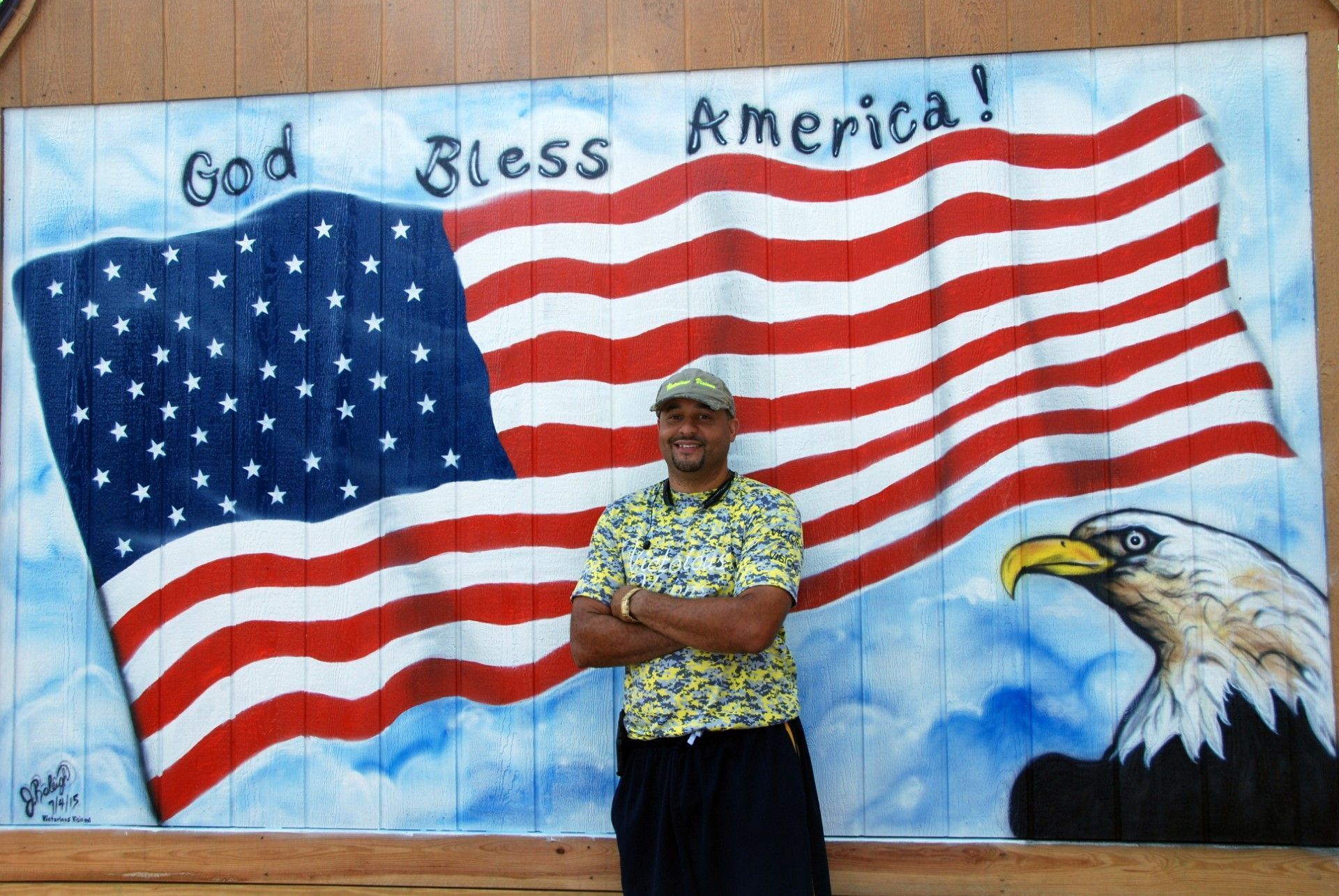 A man stands in front of a painting of an american flag and an eagle that says god bless america