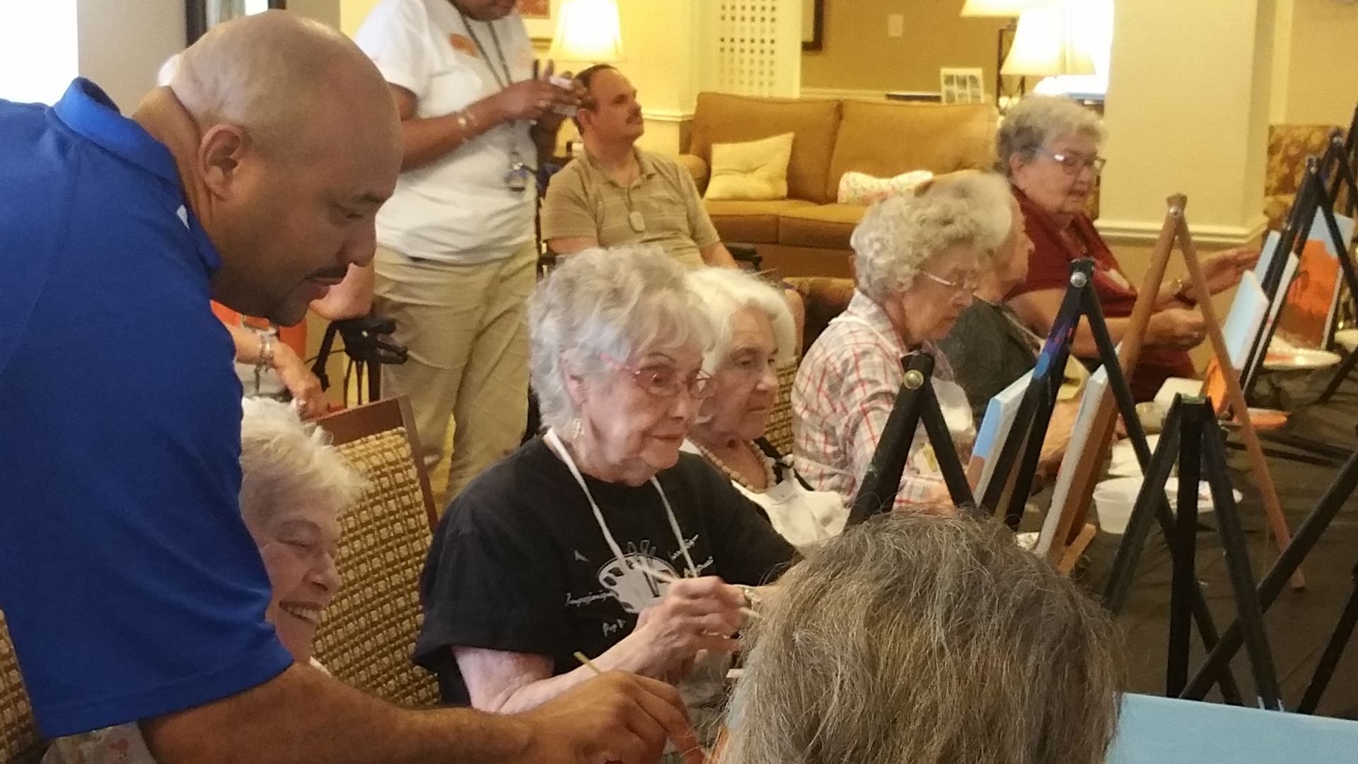 A man is teaching a group of elderly people how to paint