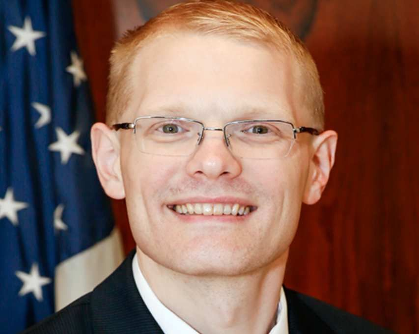 A man wearing glasses and a suit is smiling for the camera.