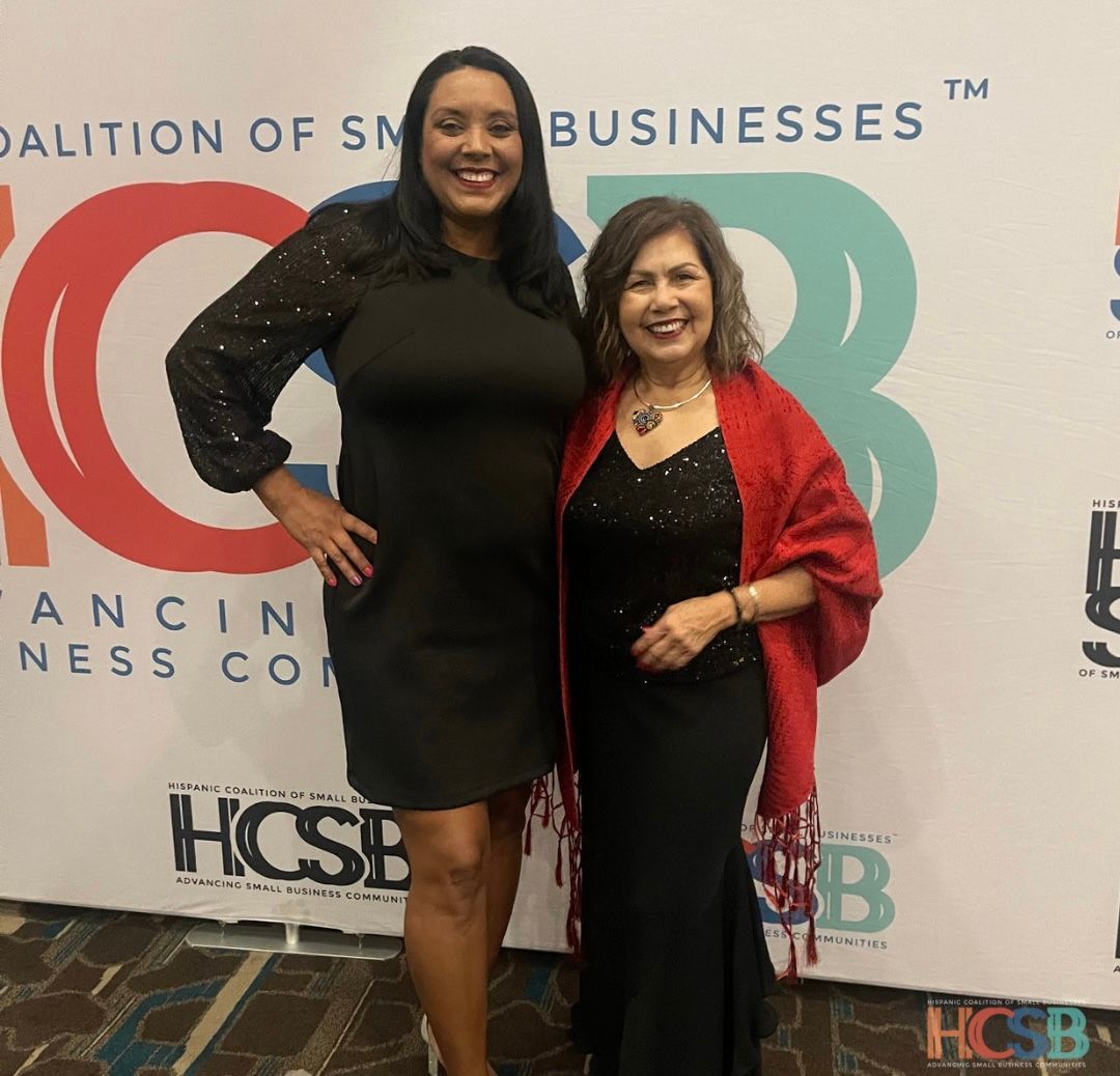 Two women standing in front of a coalition of small businesses sign