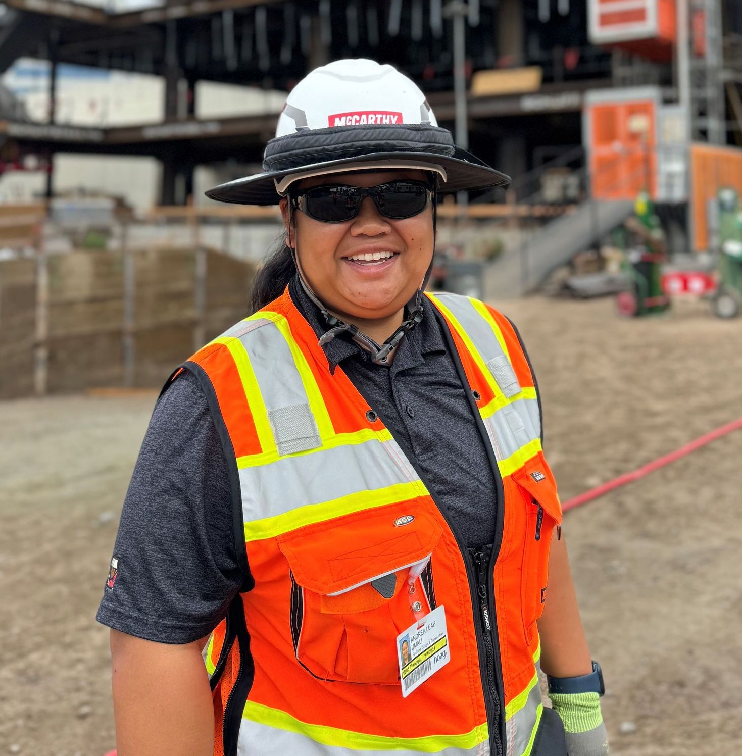 A woman wearing a hard hat and safety vest is smiling