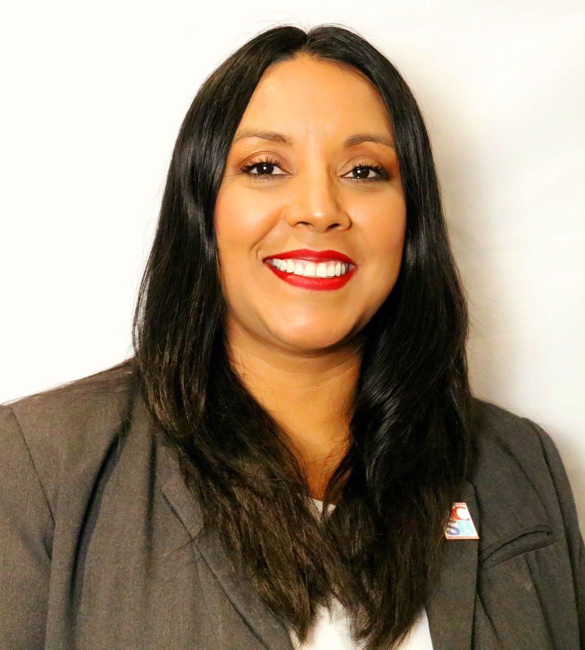 A woman wearing a pin on her jacket is smiling for the camera