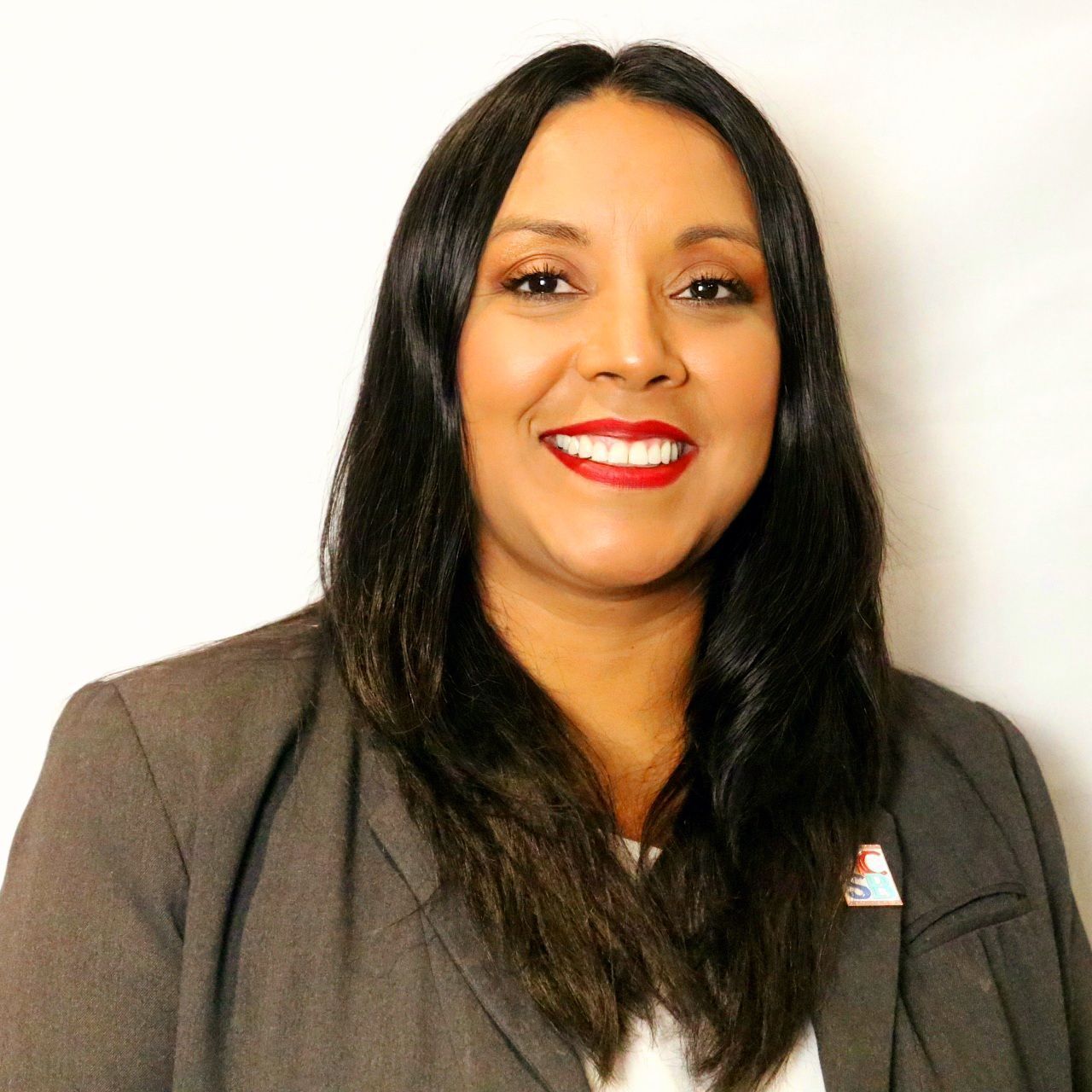 A woman wearing a blazer and red lipstick smiles for the camera