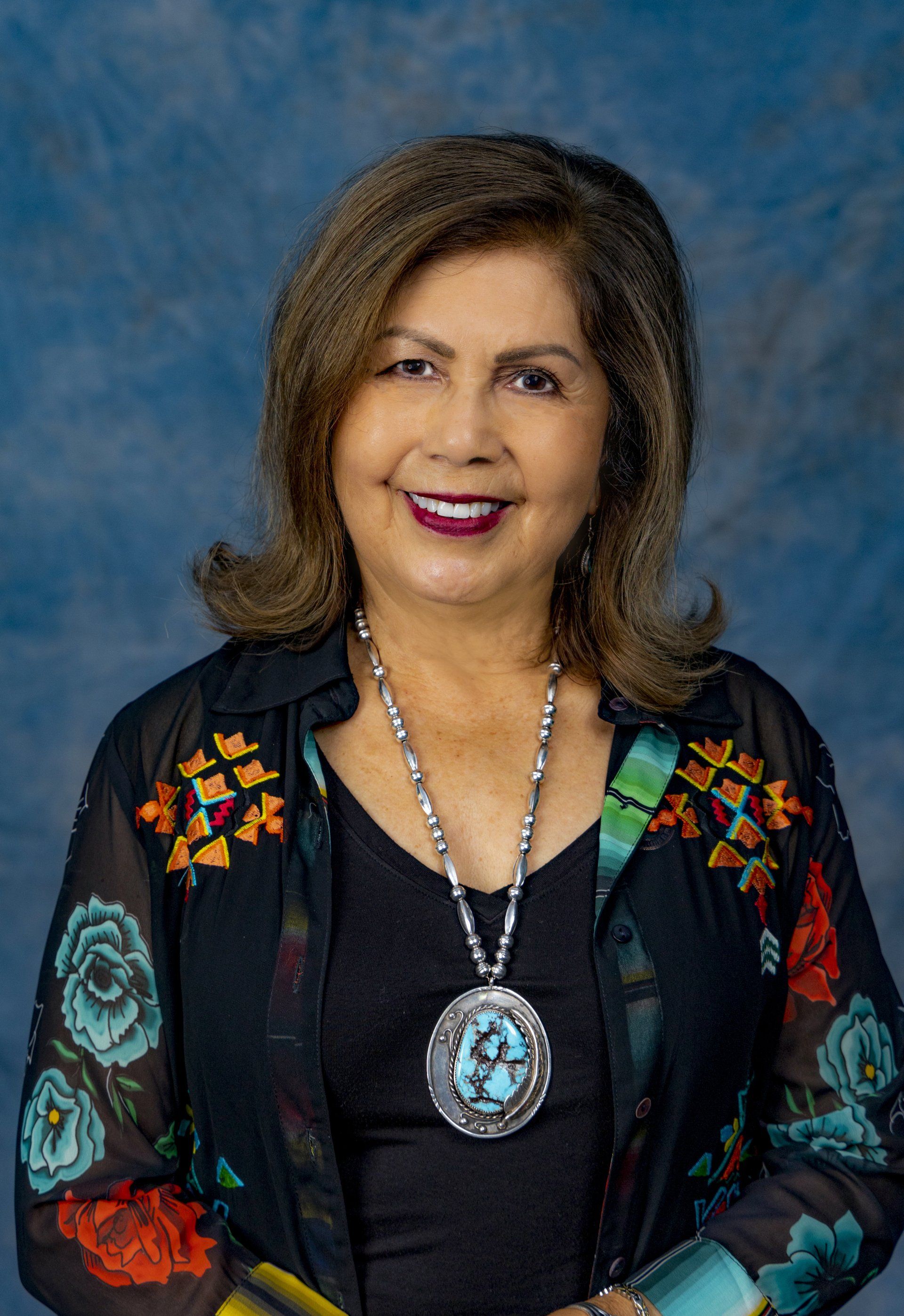 A woman wearing a floral jacket and a necklace is smiling for the camera.