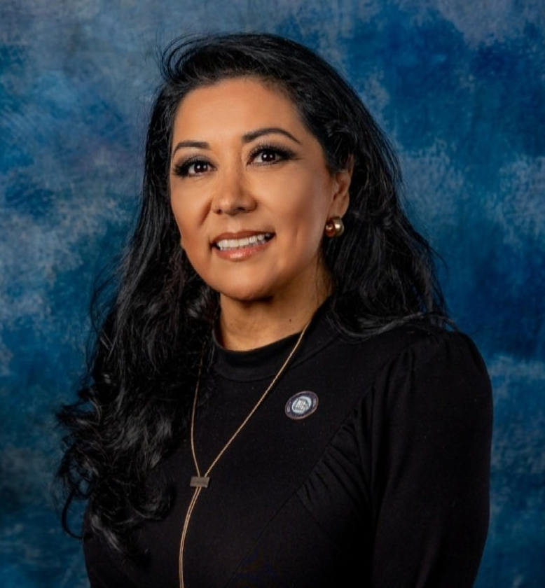 A woman wearing a black shirt and a necklace is smiling for the camera.