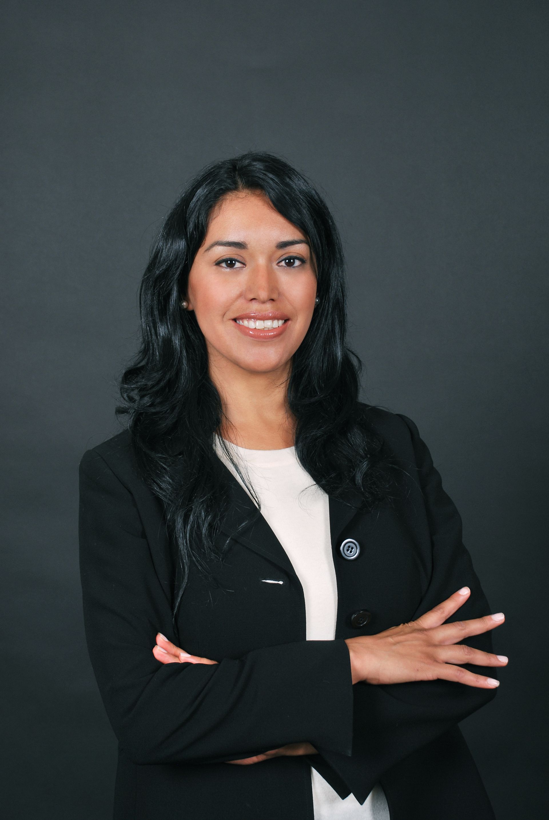 A woman in a black jacket and white shirt is posing for a picture with her arms crossed.