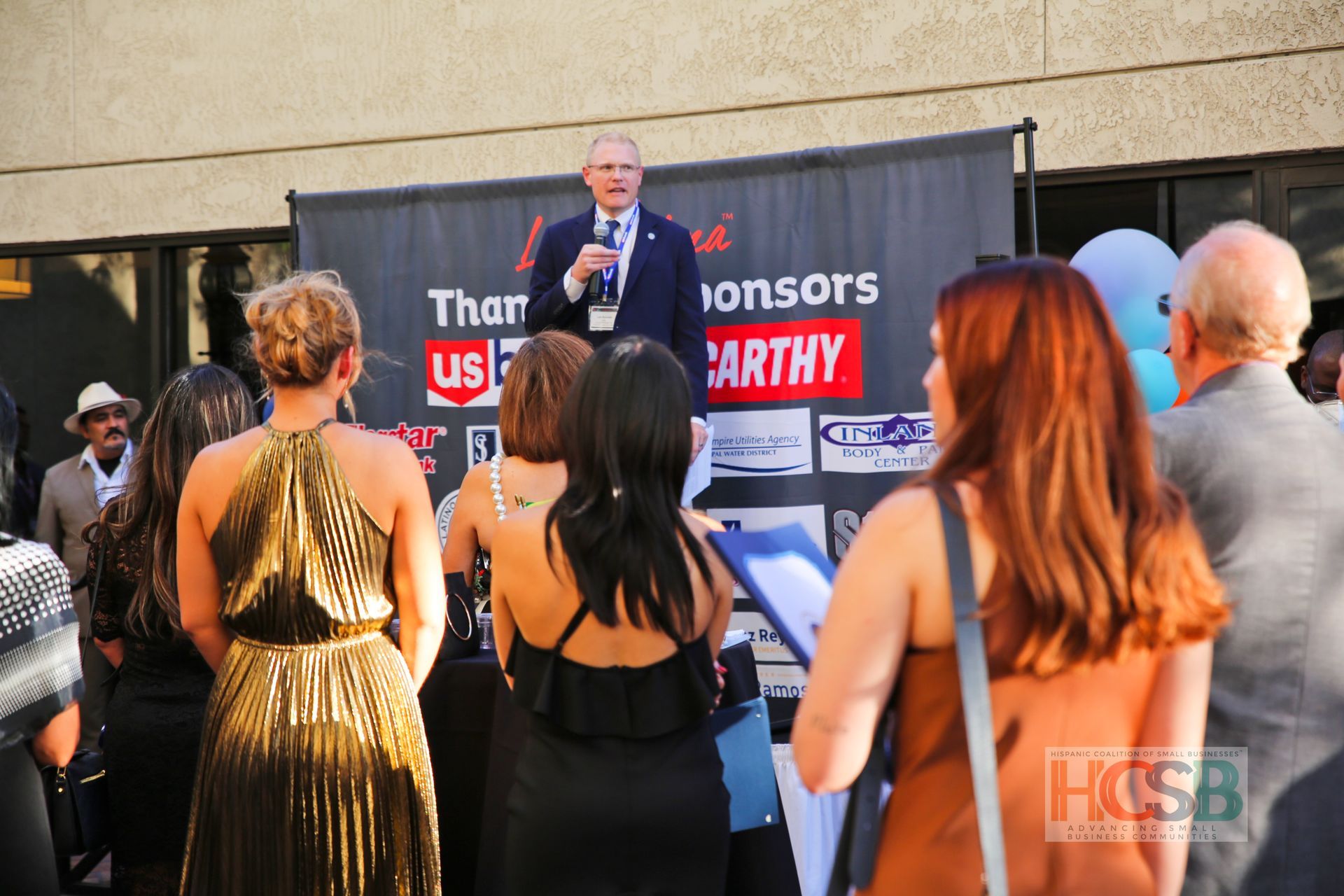 A group of people standing in front of a banner that says than us