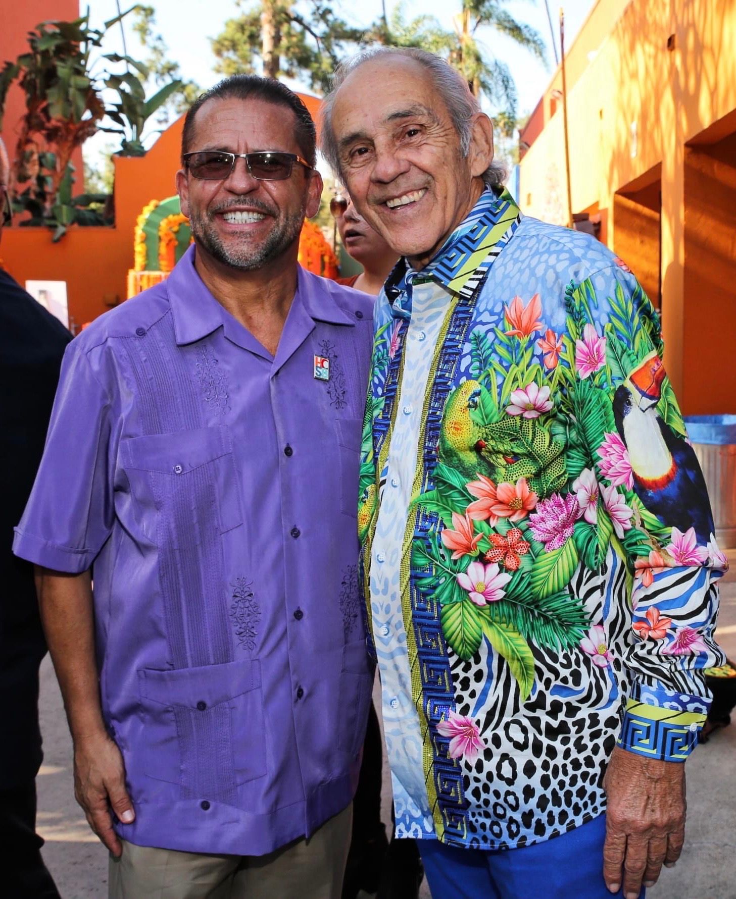 A man in a purple shirt is standing next to another man in a colorful shirt