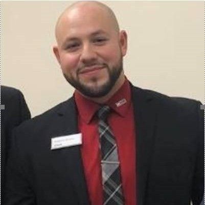 A bald man with a beard is wearing a suit and tie.