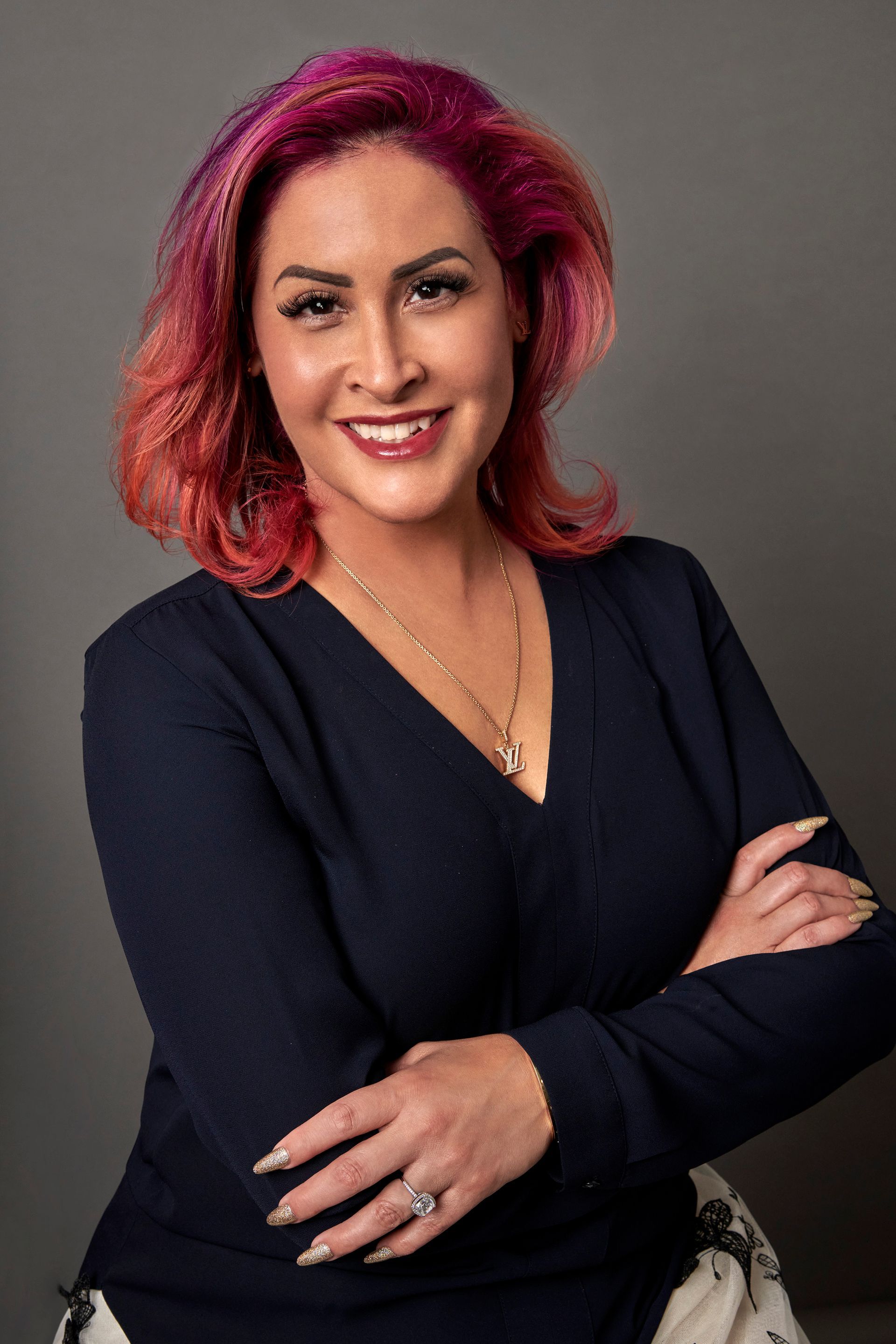 A woman with pink hair is posing for a picture with her arms crossed.