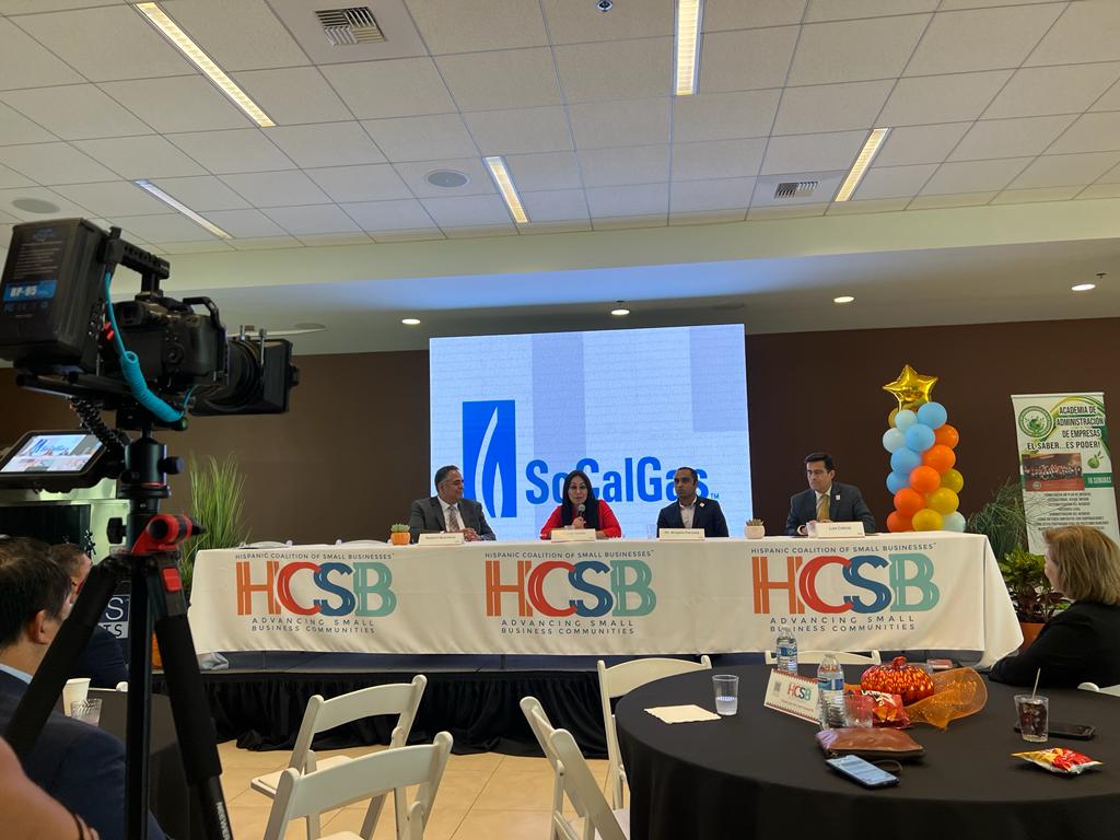 A group of people are sitting at a table in front of a large screen.