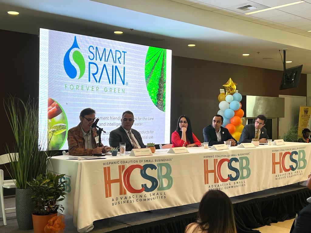 A group of people are sitting at a table in front of a large screen.