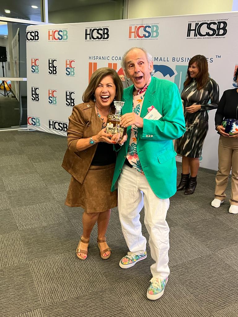 A man in a green jacket is standing next to a woman holding a trophy.