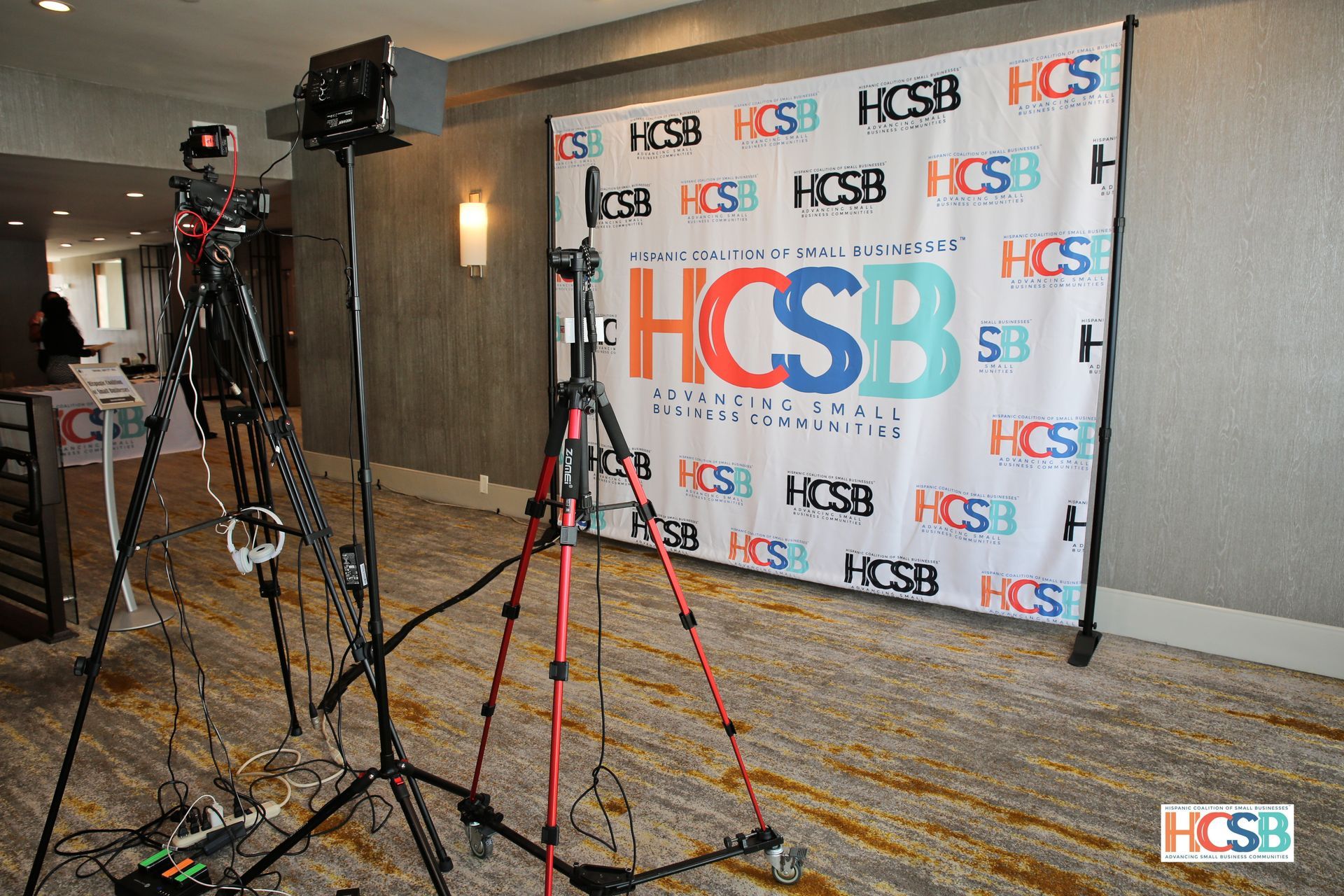 A camera is sitting on a tripod in front of a hcsb banner.