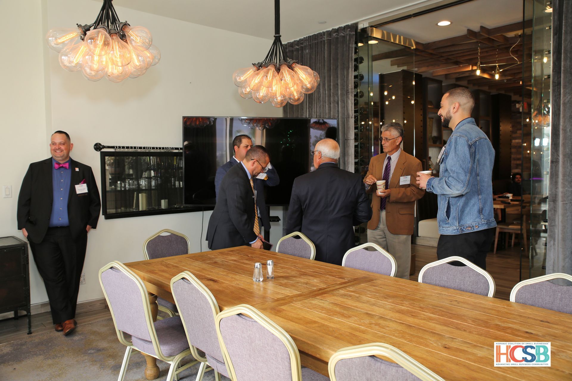 A group of men are standing around a long wooden table in a conference room.