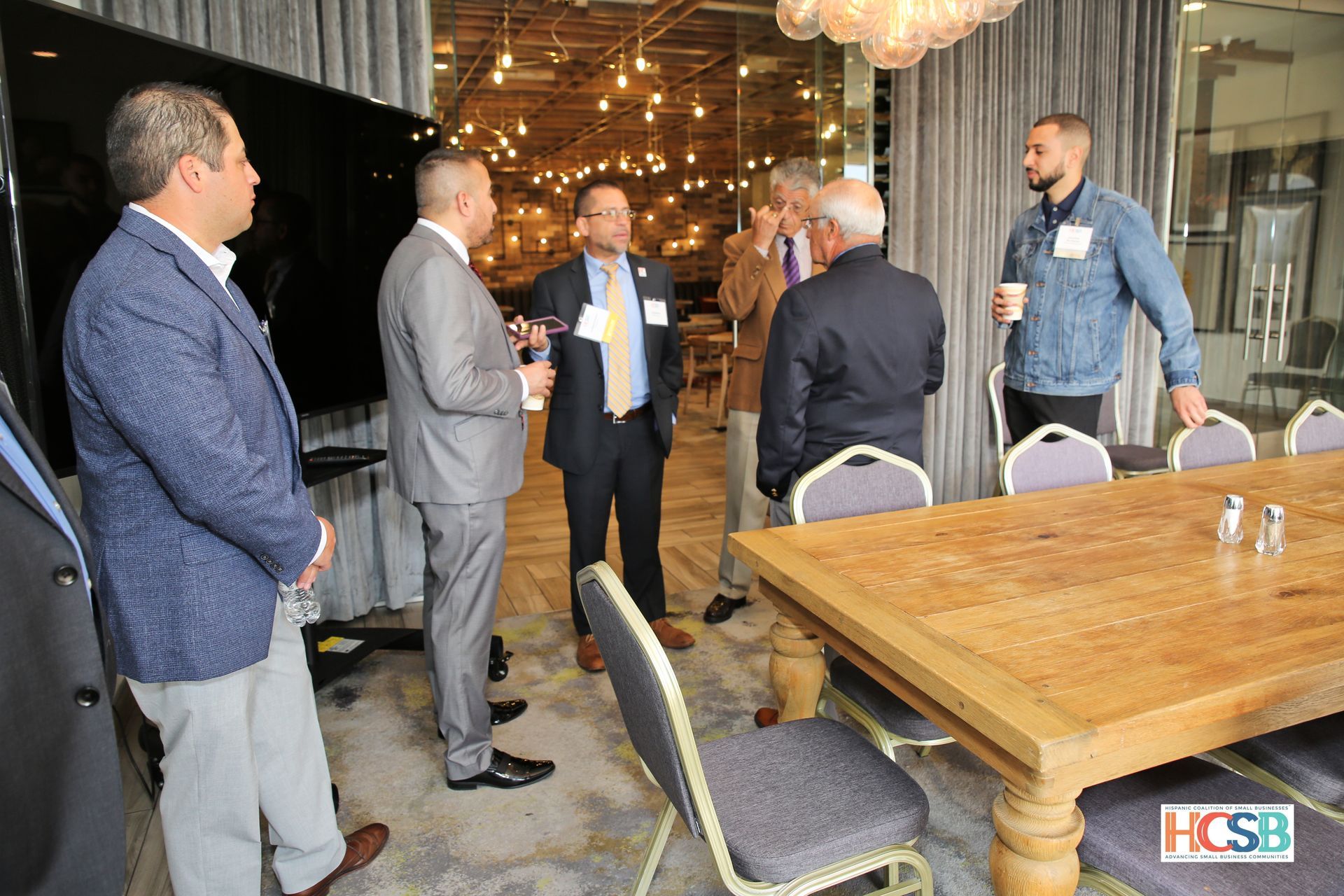 A group of men are standing around a wooden table in a conference room.