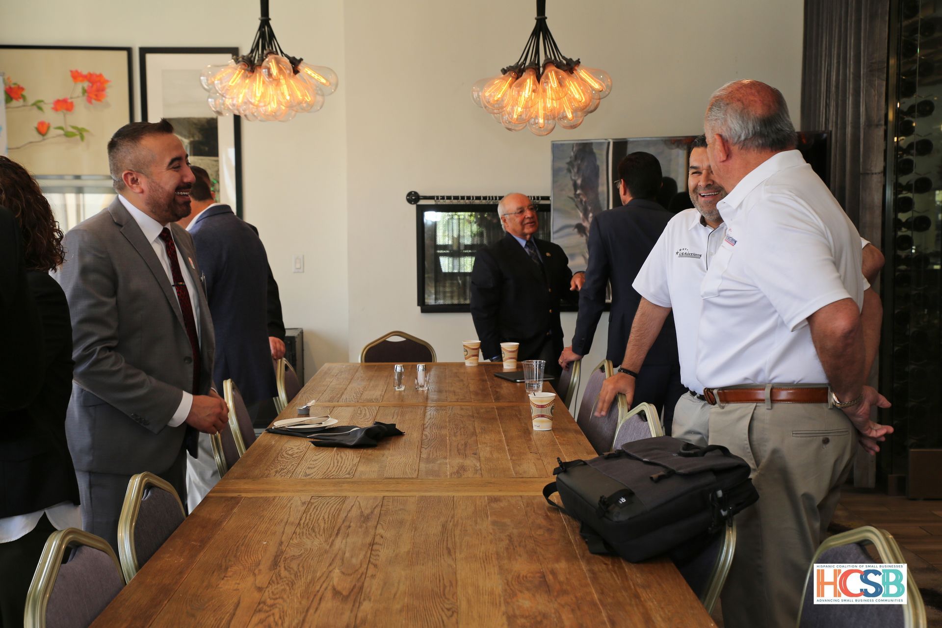 A group of men are standing around a long wooden table.