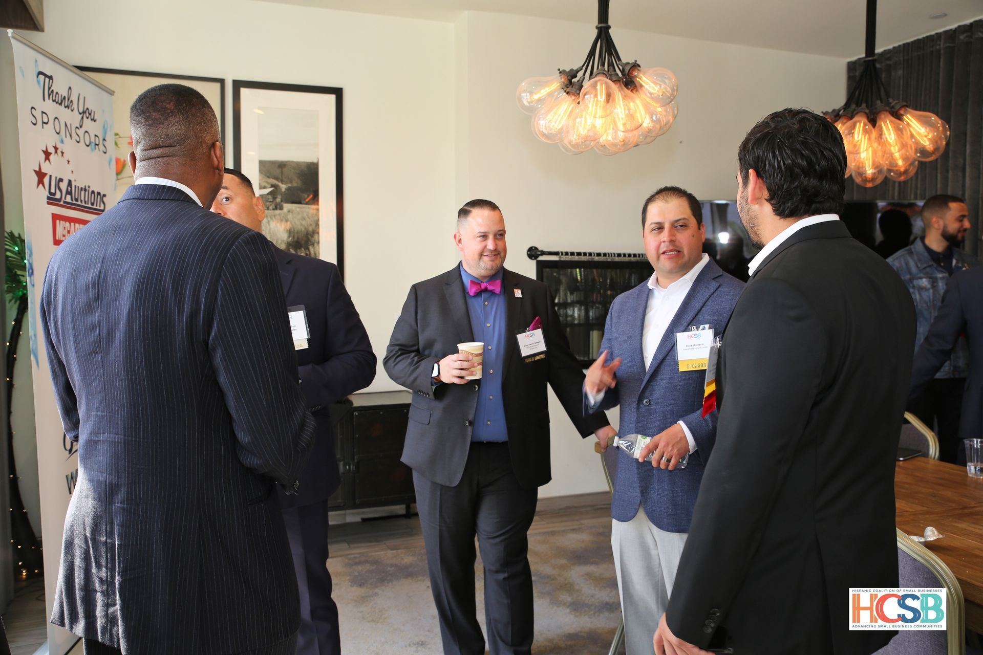 A group of men are standing in a room talking to each other.