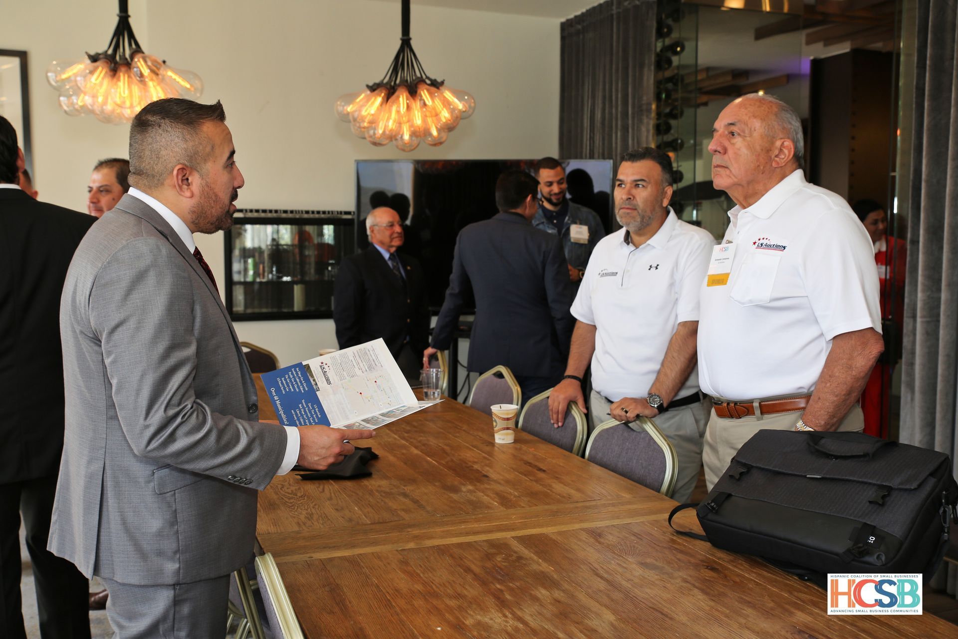 A group of men are standing around a table talking to each other.