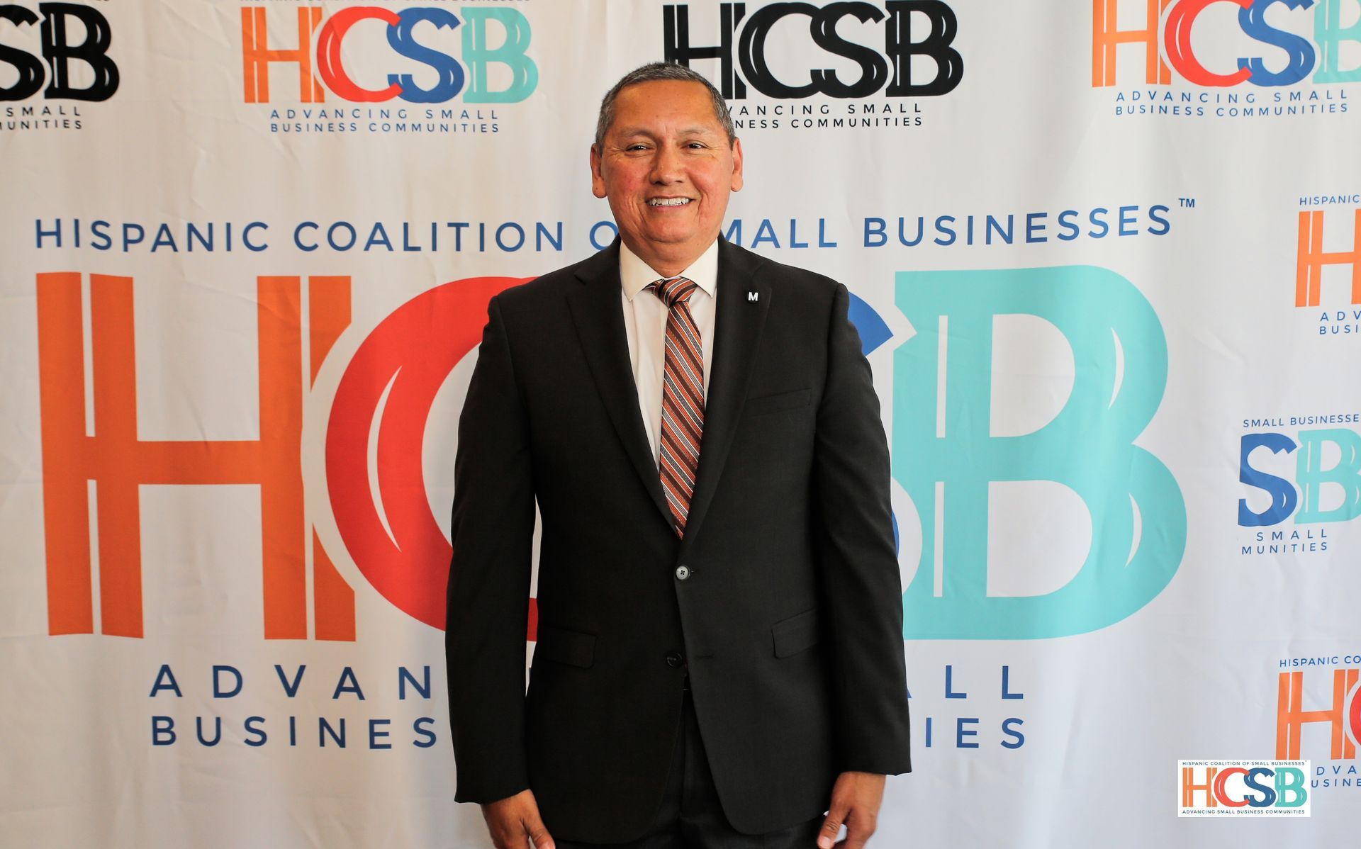A man in a suit and tie is standing in front of a hcsb banner