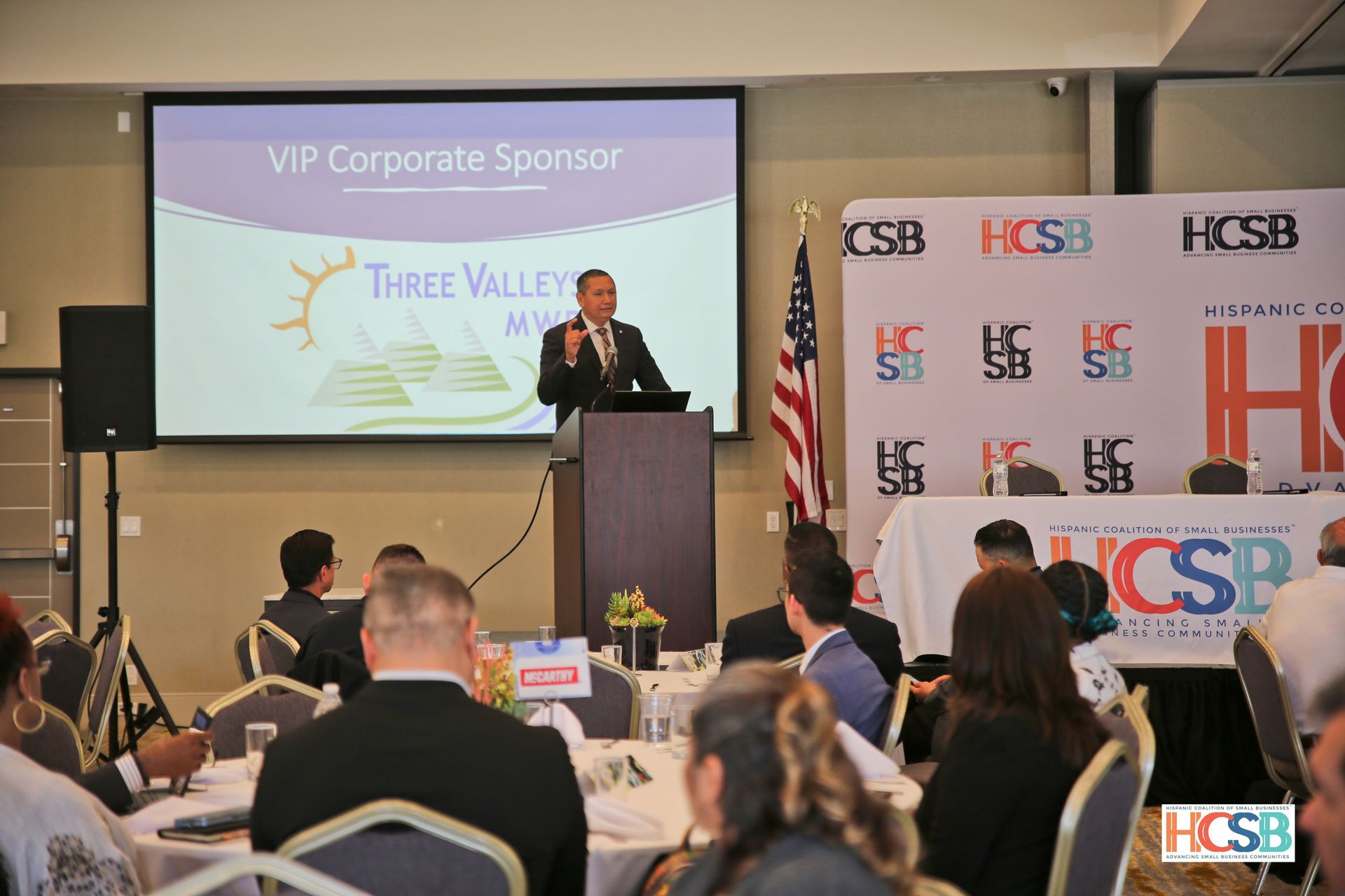A man is giving a speech in front of a large screen that says vip corporate sponsor